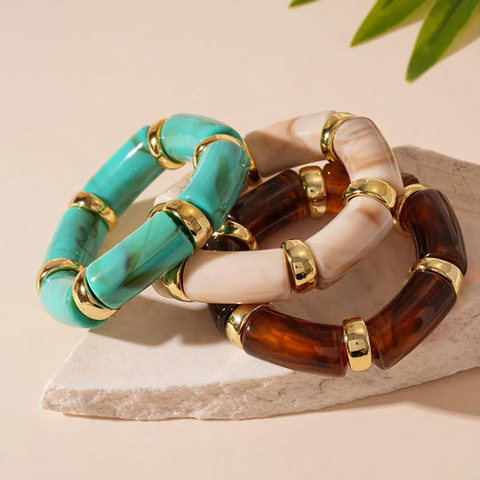 A set of three acrylic bangles in beige, brown, and turquoise colors with golden accents, displayed on a light background.