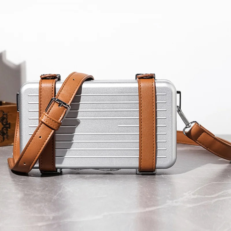 Small silver rectangular bag with brown leather straps on a light gray surface