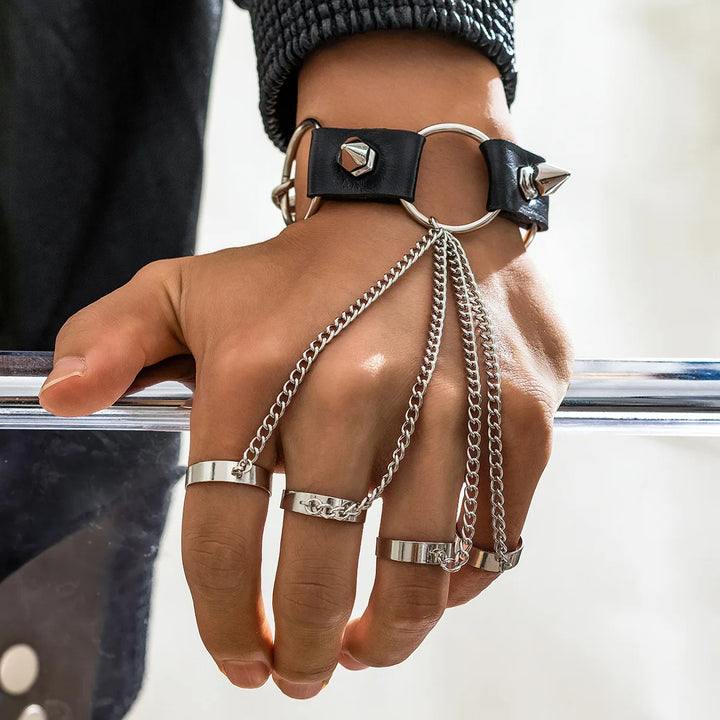 Hand with black leather wrist cuff and silver chains, wearing multiple rings.