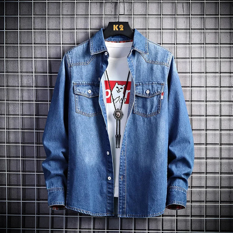 Blue denim shirt over a white t-shirt with a graphic design, worn by a mannequin against a tiled wall.