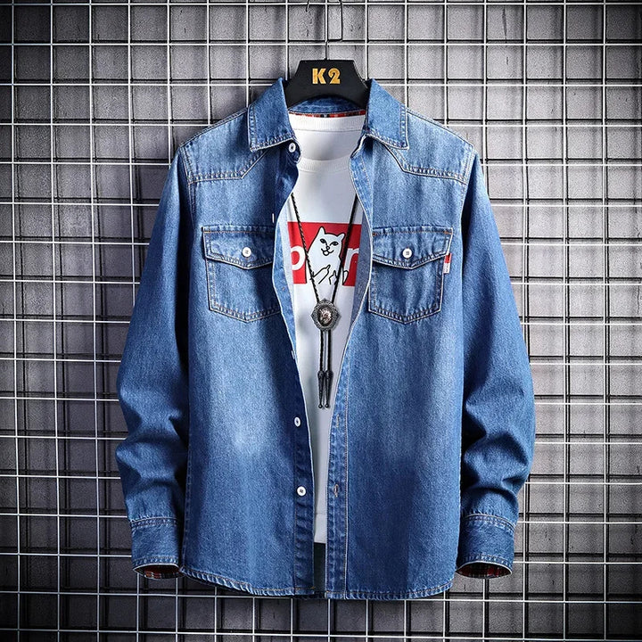 Blue denim shirt over a white t-shirt with a graphic design, worn by a mannequin against a tiled wall.