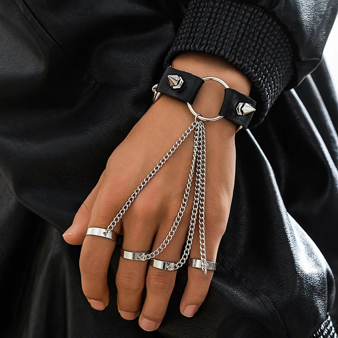 Hand wearing a black leather bracelet with silver chain and rings on a dark background