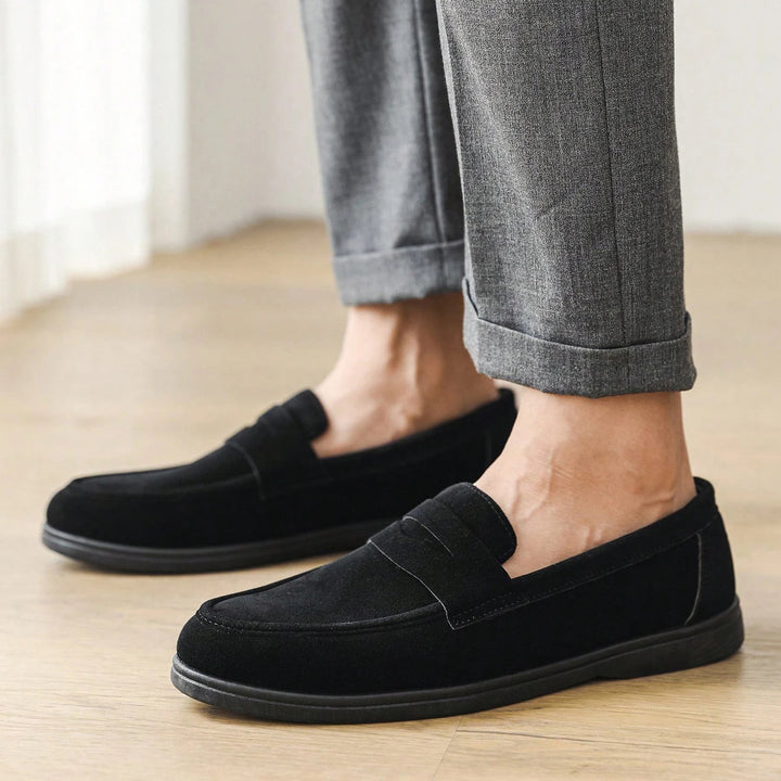 Person wearing black loafers and gray pants on a wooden floor.