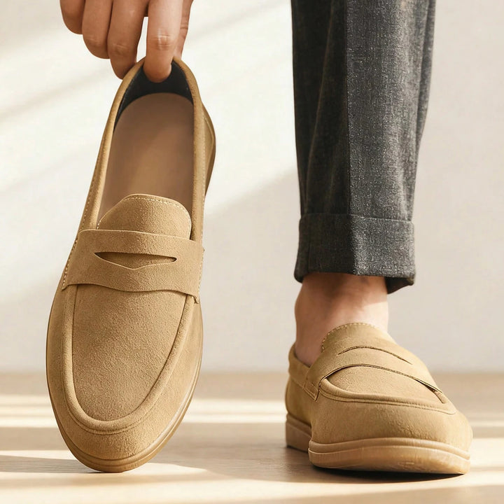 Tan loafers being held up with a neutral background