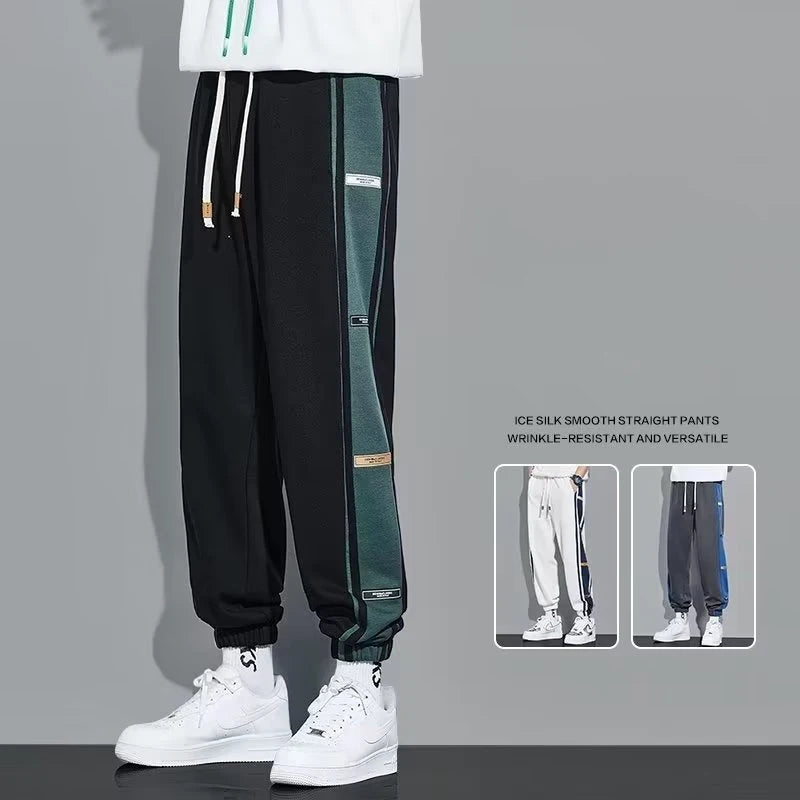 Person wearing black and green pants with white sneakers on a gray background
