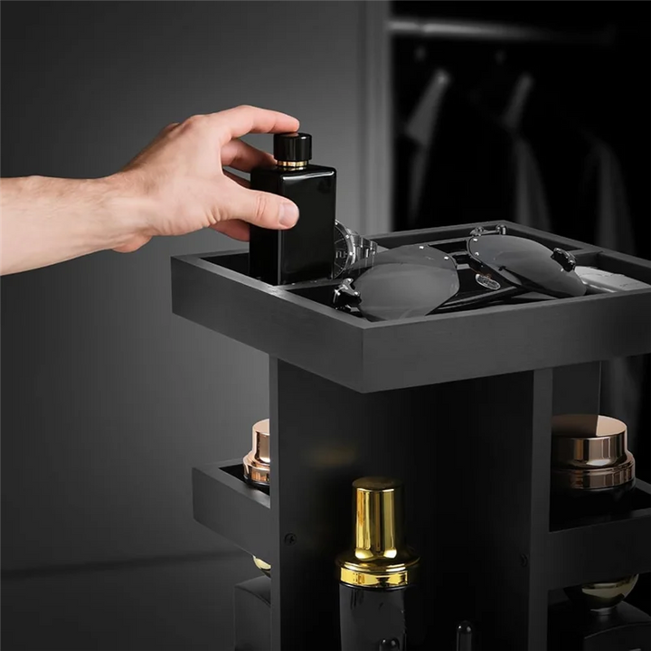 Hand reaching for a black perfume bottle on a dark shelf with other bottles and containers.