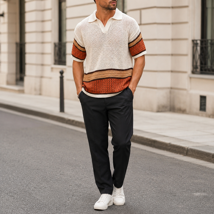 Man wearing a patterned sweater and black pants standing on a street.