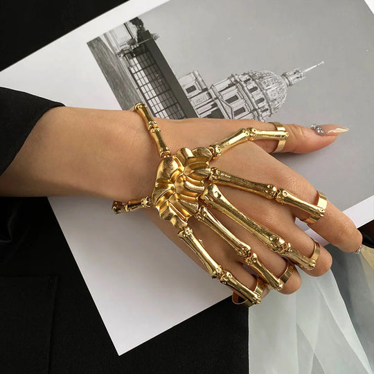 Gold skeleton hand bracelet and ring on a hand with a blurred architectural background