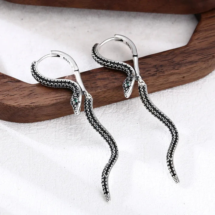 A pair of drop earrings in the shape of sculpted snakes, crafted from high-polish 925 sterling silver with black pavé detailing.