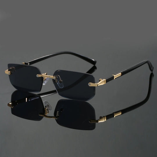 A pair of rimless sunglasses with cut-edge lenses and a frameless design. The sunglasses are black with gold accents on the hinges and corners.