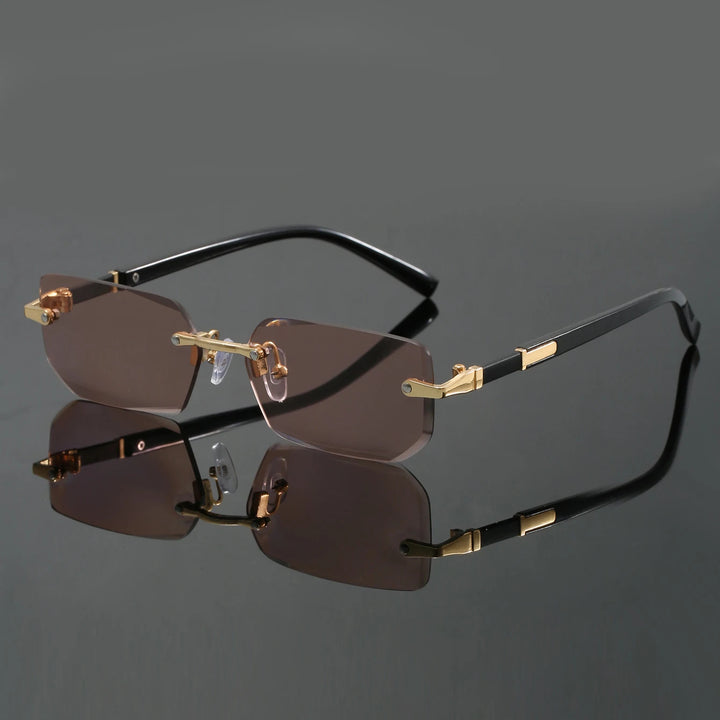 A pair of rimless sunglasses with cut-edge lenses and a frameless design. The sunglasses are black with gold accents on the hinges and corners.