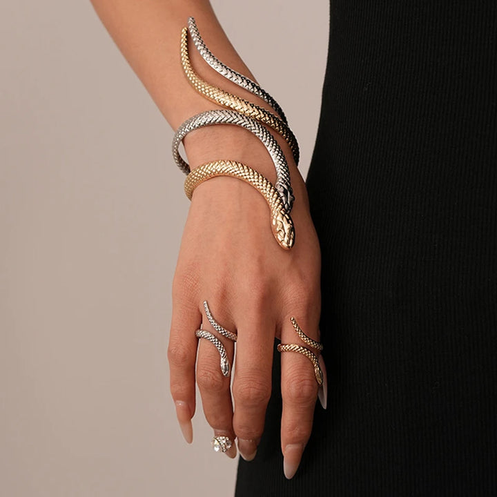Hand wearing multiple gold and silver bracelets and rings on a neutral background