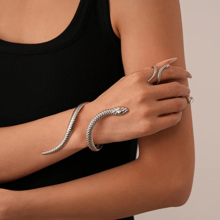 Person wearing a silver snake bracelet and ring on a neutral background